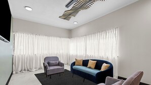 Ein modernes Zimmer mit einer Couch, zwei Sesseln, einem schwarzen Teppich und transparenten Vorhängen.