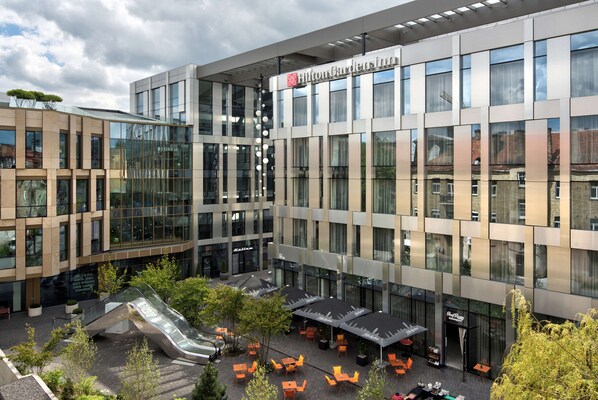 Un hôtel moderne doté d’une façade en verre, d’un espace extérieur aménagé et d’un escalier apparent.