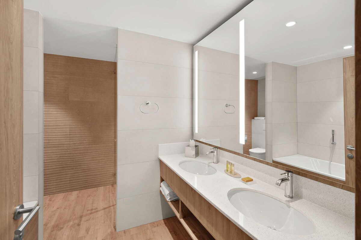 A modern bathroom with two sinks, a large mirror, and a shower area.