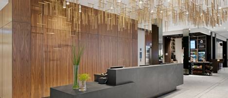 A modern reception area with a wooden panel wall, a dark reception desk, and a hanging light fixture.