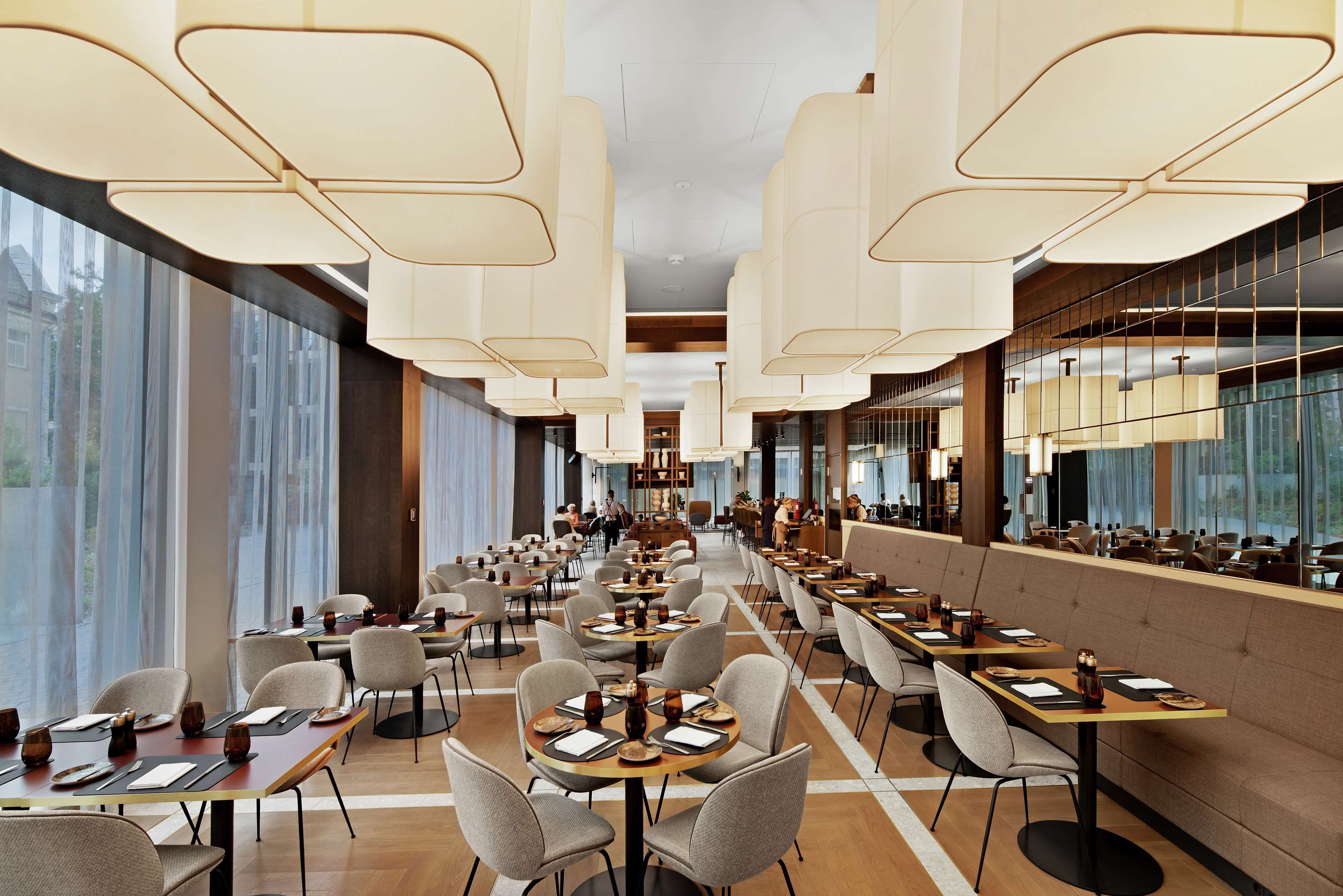 Un vaste espace de restauration d’hôtel, doté de longues tables, d’un éclairage moderne suspendu et de grandes fenêtres offrant une vue panoramique.