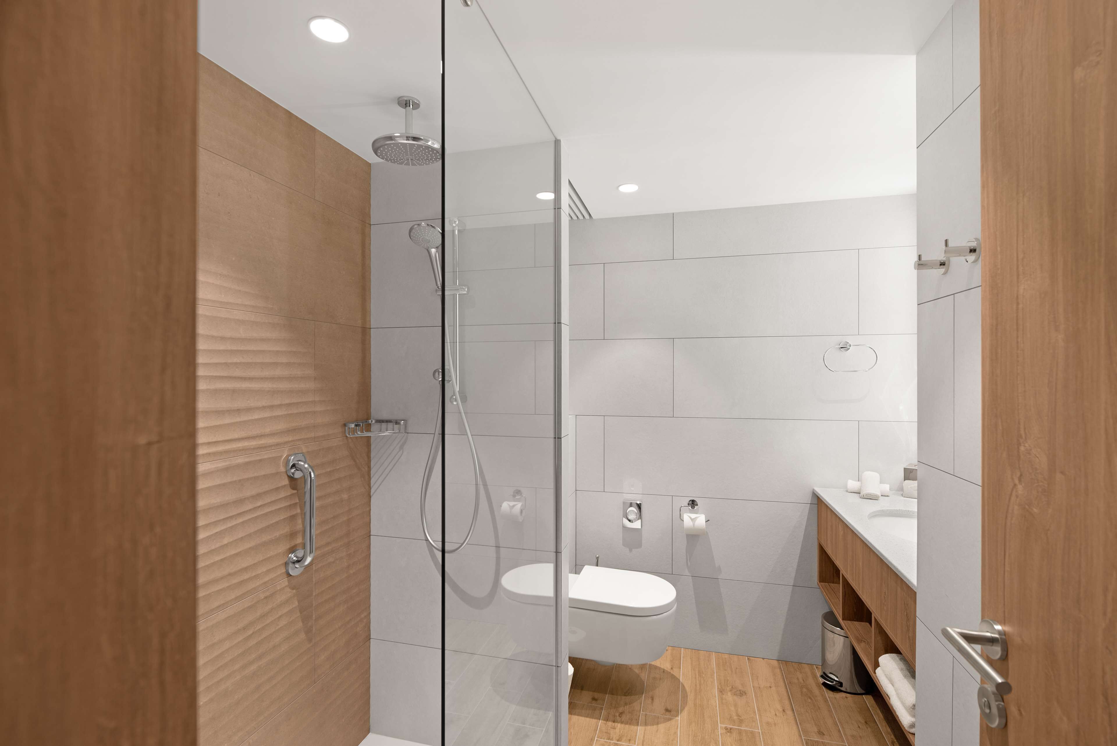 A modern bathroom with a glass-enclosed shower, a white toilet, and a wooden vanity.