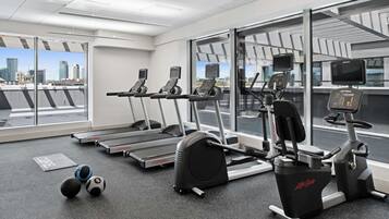Un gimnasio con cintas de correr, elíptica y bicicleta estática, con vistas a la ciudad a través de amplias ventanas.
