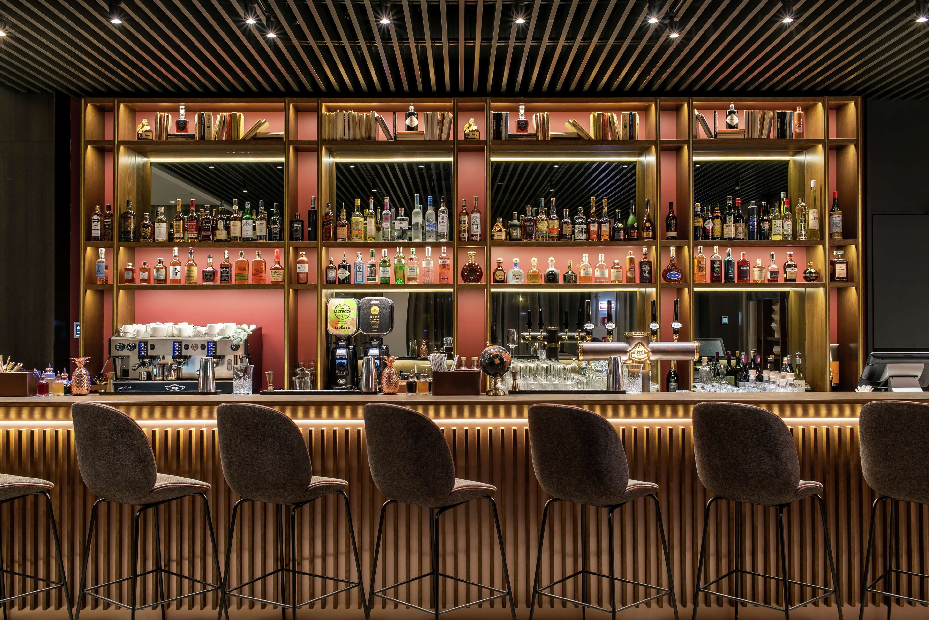 A bar area with multiple shelves of liquor bottles, a coffee machine, and bar stools.