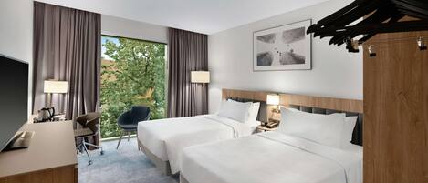 Una habitación de hotel con dos camas, un escritorio, una silla, un televisor y una ventana con cortinas.