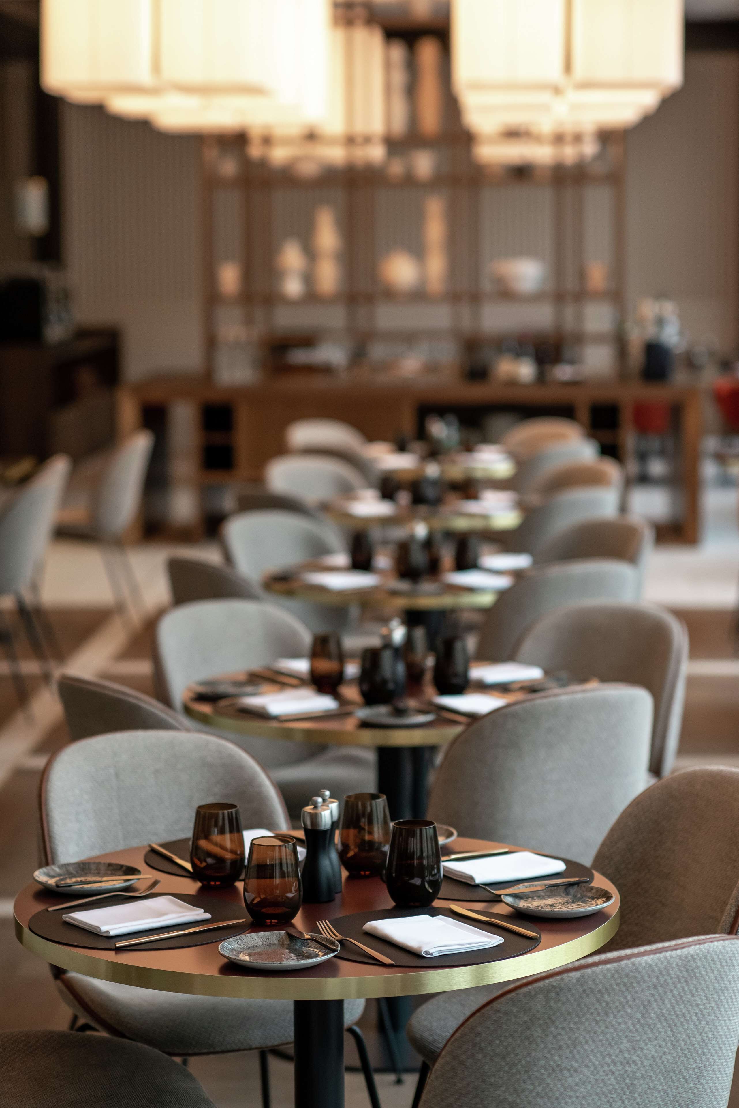 A restaurant with round tables set with plates, glasses, and cutlery.