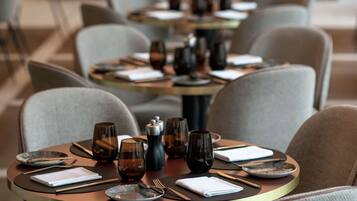 A restaurant with round tables set with plates, glasses, and cutlery.