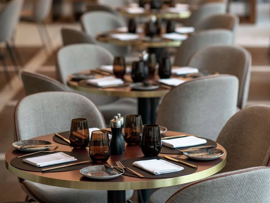 A restaurant with round tables set with plates, glasses, and cutlery.