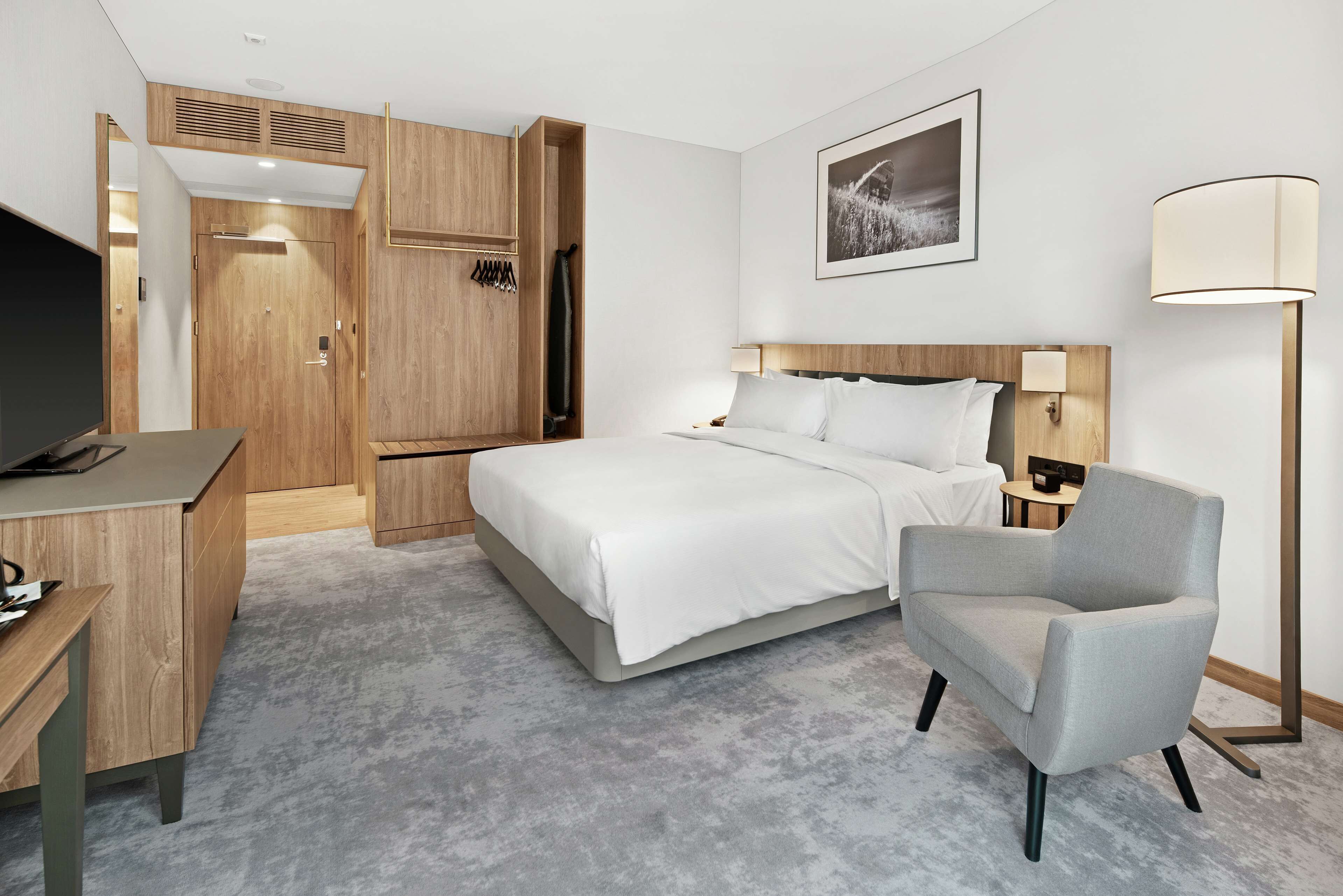 A hotel room with a bed, a desk, a chair, a TV, and a lamp.