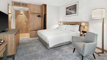 A hotel room with a bed, a desk, a chair, a TV, and a lamp.