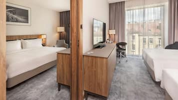 Habitación de hotel con dos camas, un escritorio, una silla, un televisor y una ventana con vista a edificios.