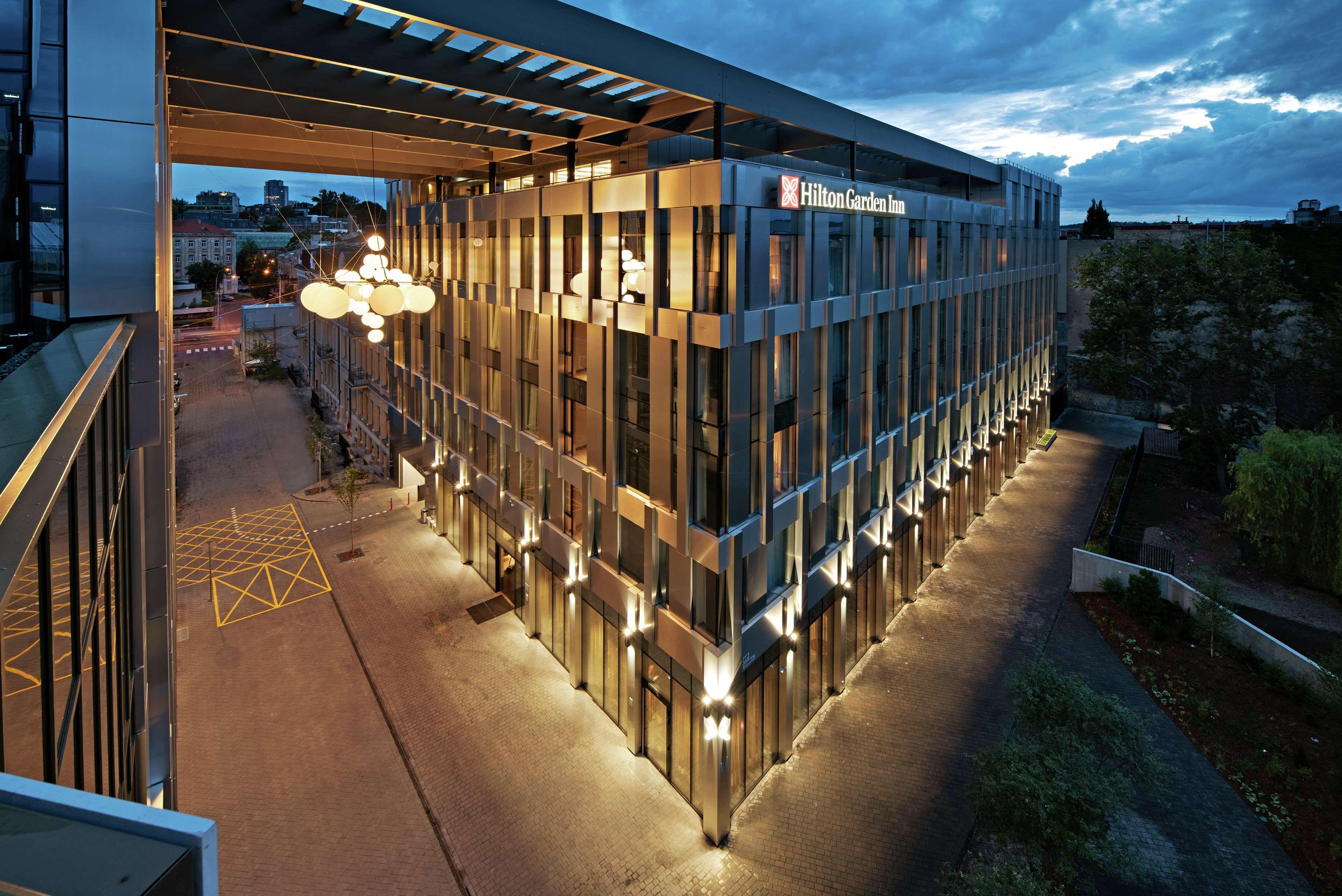 Un hotel moderno con facciata in vetro, illuminato da luci interne, e un ingresso visibile con una tettoia.