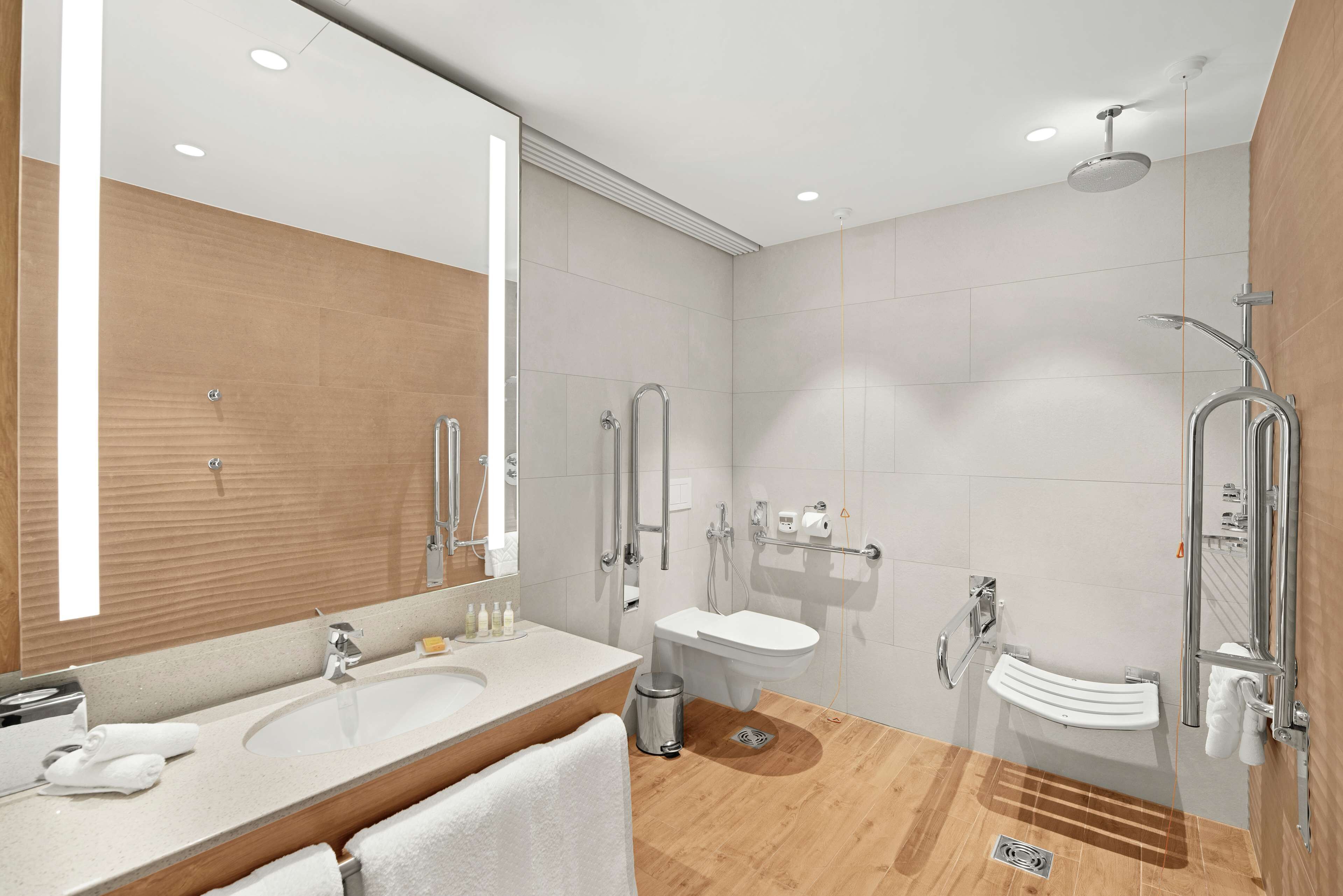 A modern bathroom with a large mirror, two sinks, a shower, and a toilet.