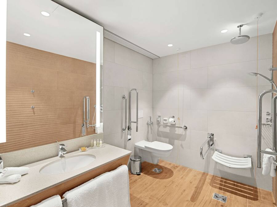 A modern bathroom with a large mirror, two sinks, a shower, and a toilet.