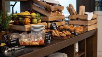 A breakfast buffet with various fruits, pastries, and a coffee station.