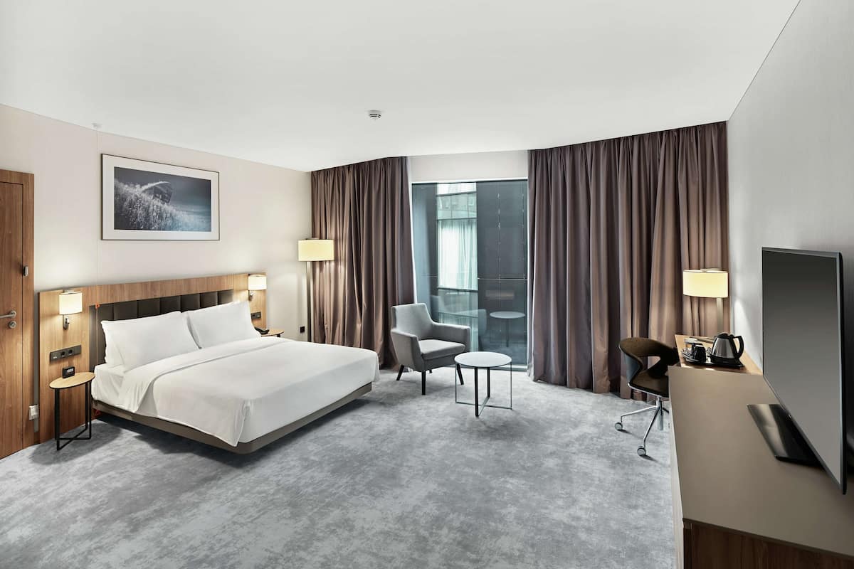 A modern hotel room with a large bed, a desk, a chair, and a TV.