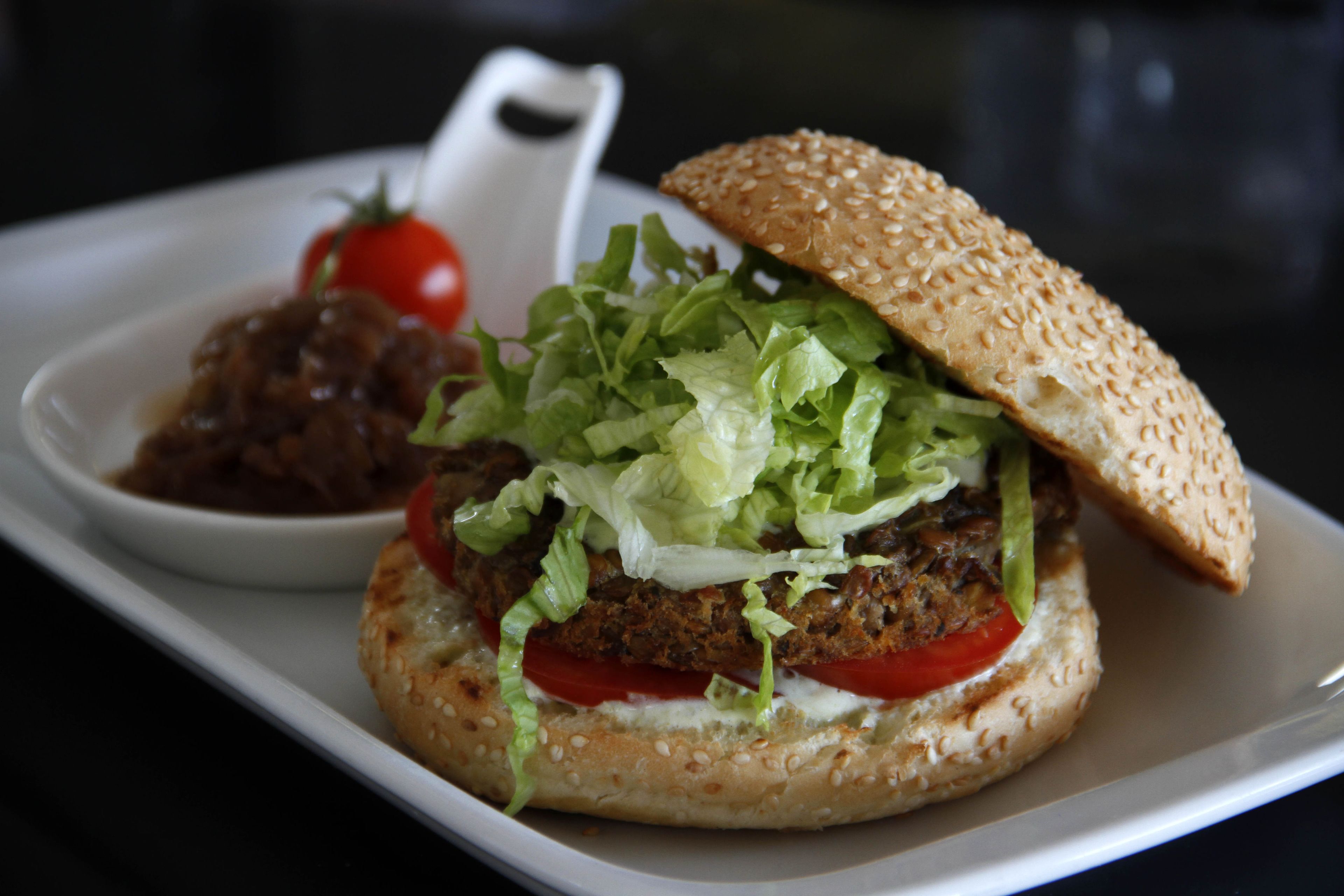 Hamburguesa con lechuga, tomate y pan con semillas de sésamo sobre un plato blanco.
