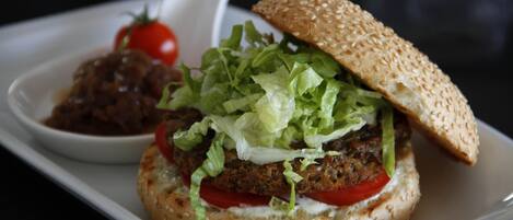 A burger with lettuce, tomato, and a sesame seed bun on a white plate.