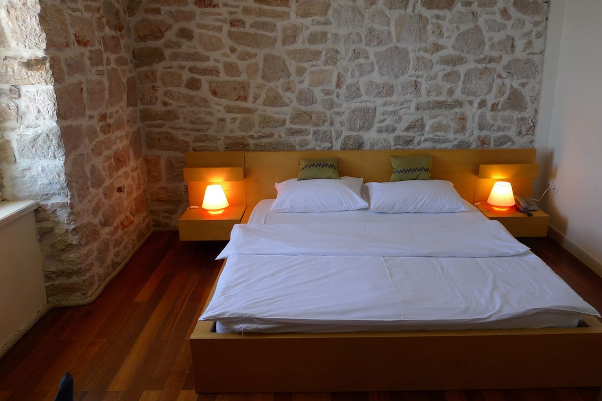 A bed with white linens in a room with stone walls and wooden flooring.