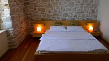 Una cama con sábanas blancas en una habitación con paredes de piedra y suelo de madera.