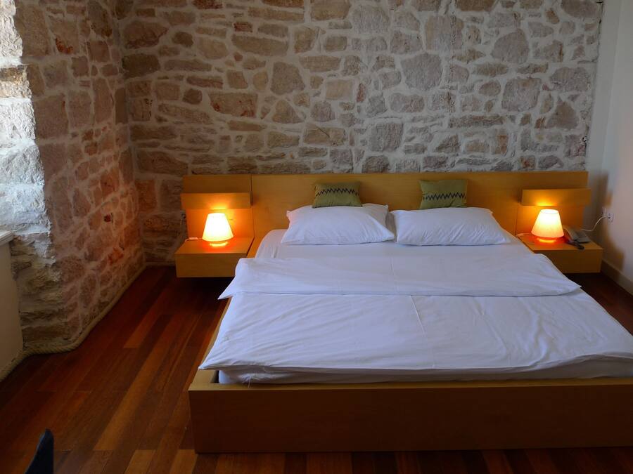 Una cama con sábanas blancas en una habitación con paredes de piedra y suelo de madera.