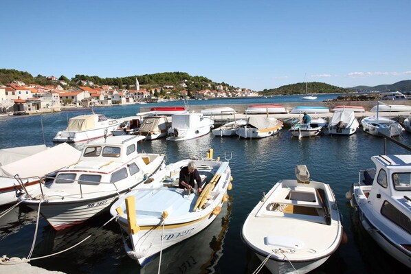 A marina with various boats docked, a person on a boat, and a coastal town in the background.