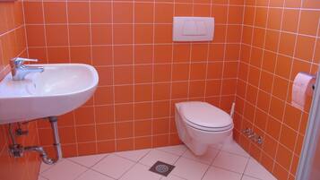 A small bathroom with an orange tiled wall, a white sink, and a toilet.