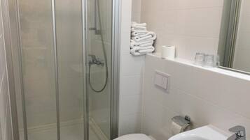 Un baño moderno con ducha envuelta en vidrio, inodoro blanco y lavamanos con espejo superior.