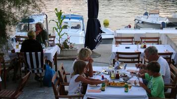 An outdoor dining area with tables and chairs, overlooking a body of water with boats.