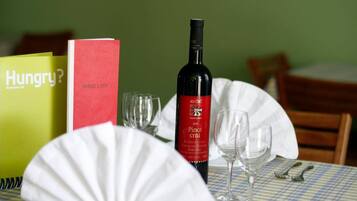 A dining table with a checkered tablecloth, a wine bottle, wine glasses, a menu, and a painting on the wall.