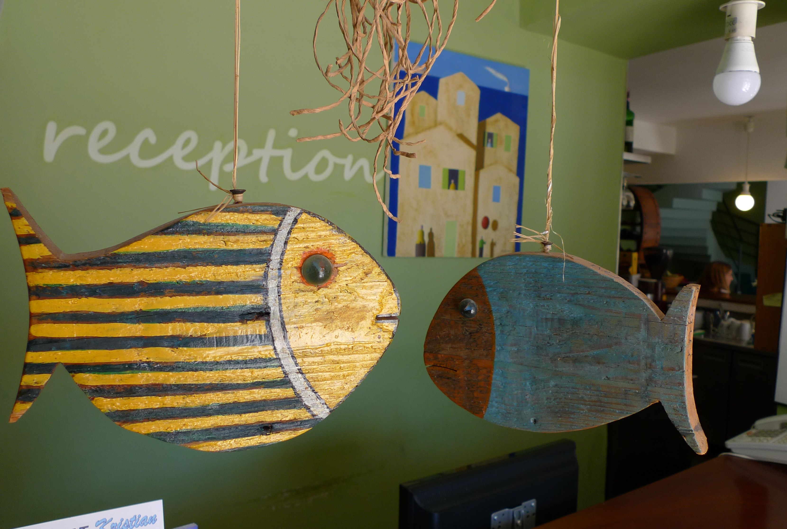 Two wooden fish decorations hanging from the ceiling in a room with a green wall and a reception sign.