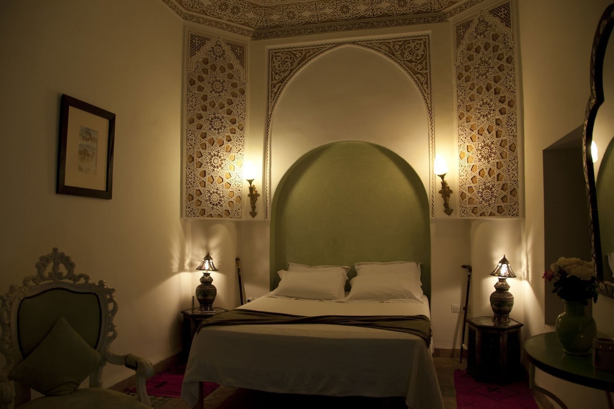 Una habitación con una cama, decoraciones ornamentales en las paredes y dos lámparas de pared.