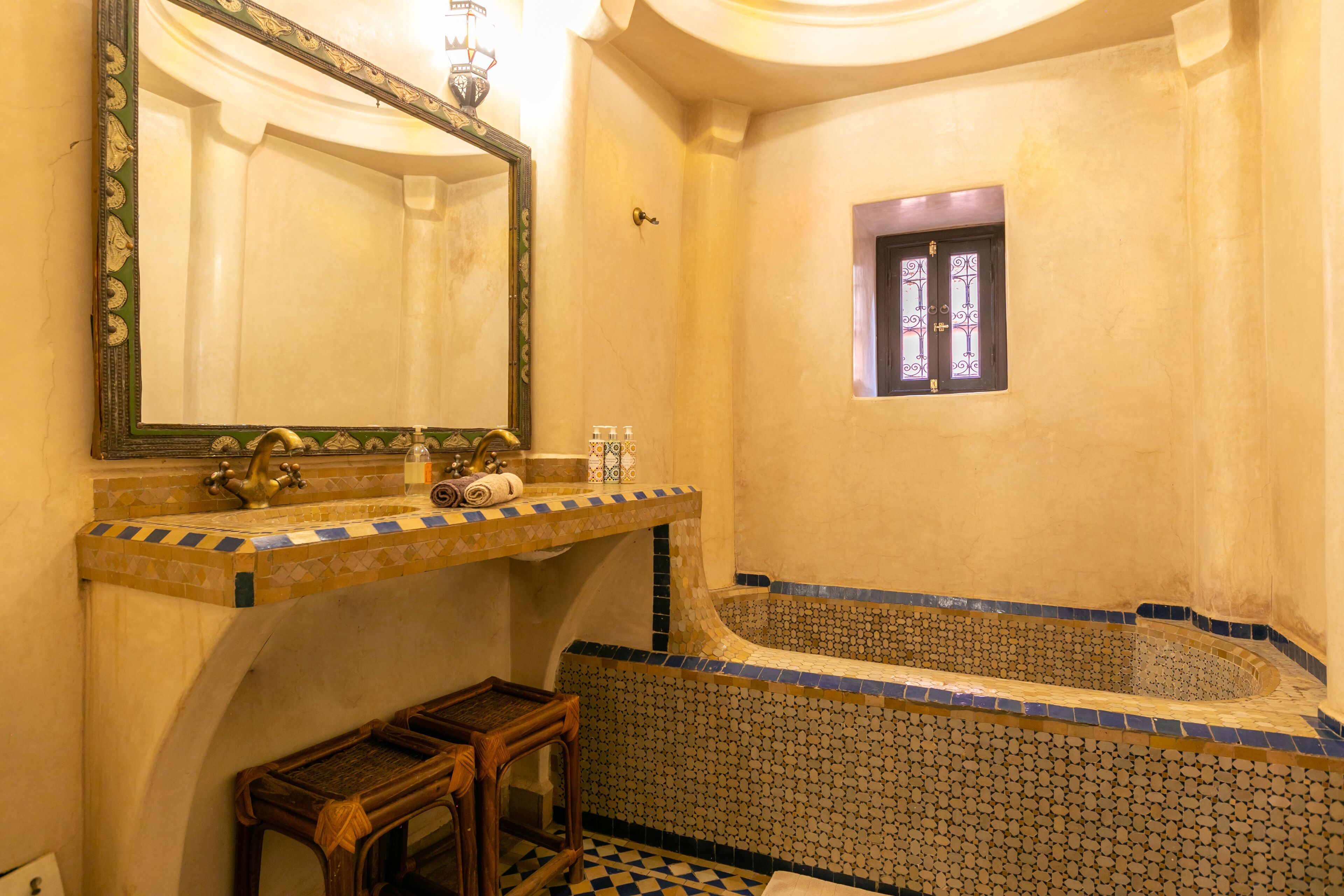 A bathroom with a bathtub, a sink with a mirror, and a window with decorative glass.