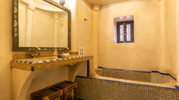 A bathroom with a bathtub, a sink with a mirror, and a window with decorative glass.
