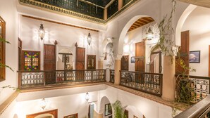 Interior con varios niveles, arcos, barandas de madera y plantas colgantes.