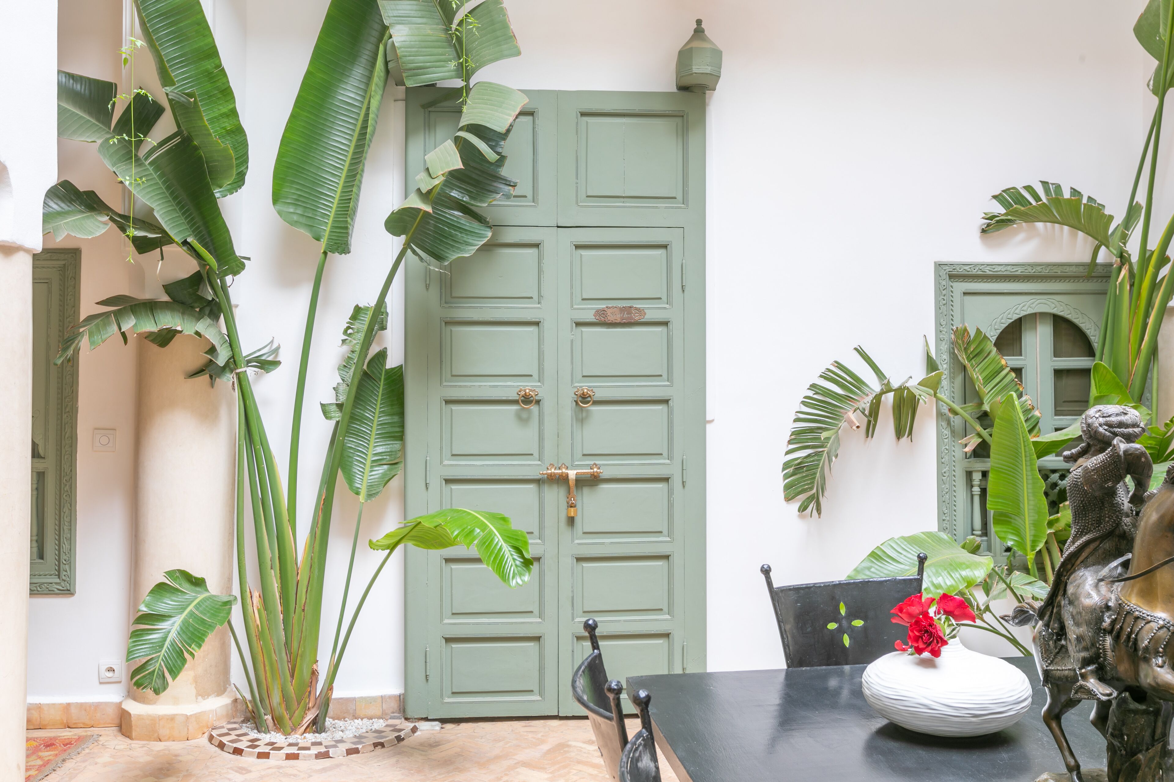 Una habitación con una puerta verde, plantas grandes, una mesa negra y una estatua decorativa de un caballo.