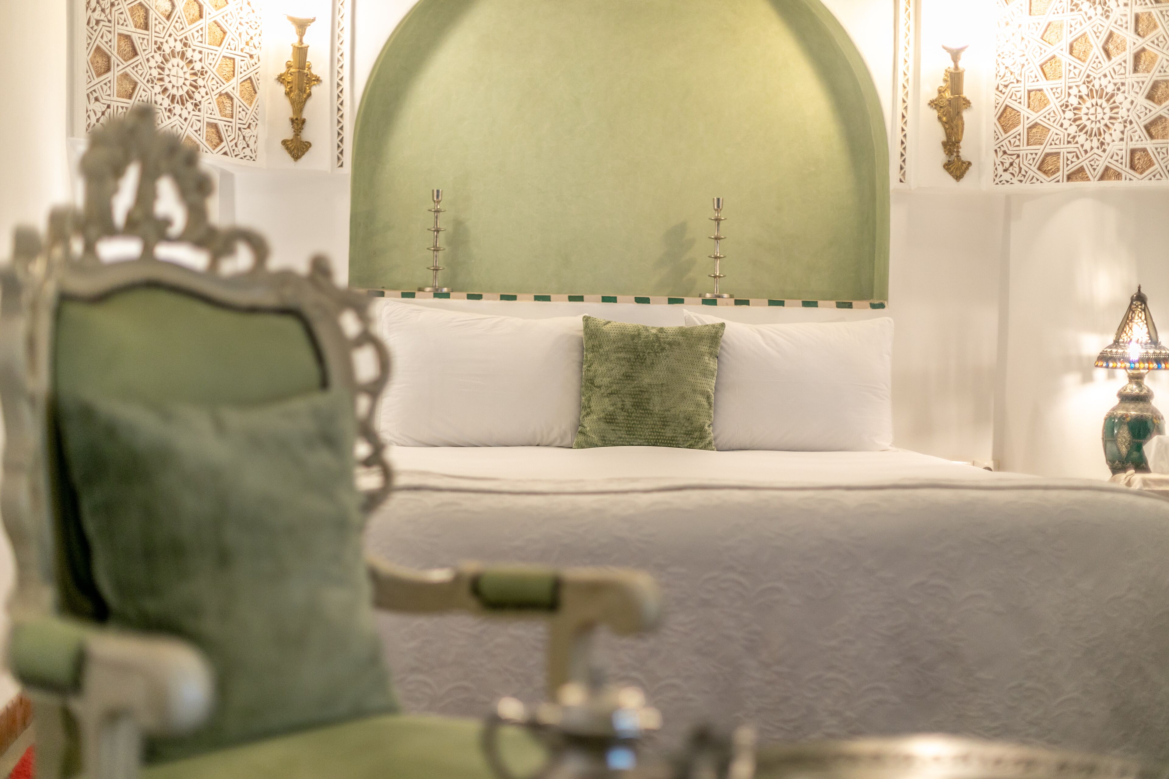 A bed with a green headboard, white bedding, and a decorative pillow.