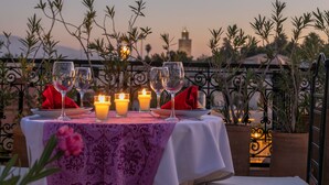 Una mesa para dos, con velas, copas y un mantelino rojo, con vista a un paisaje urbano al anochecer.