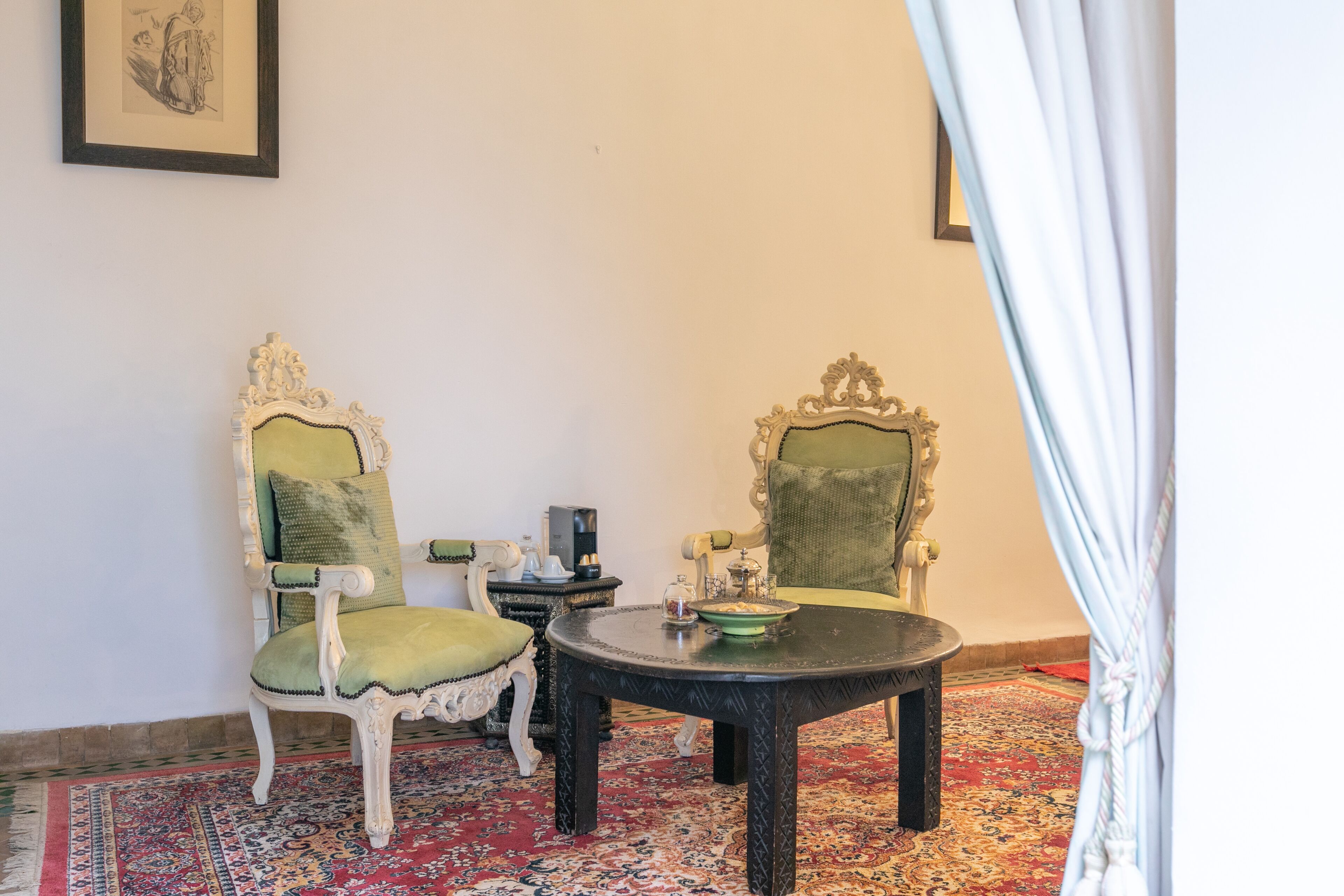 Una habitació amb dues cadires decorades, una taula rodona i una catifes amb motius.