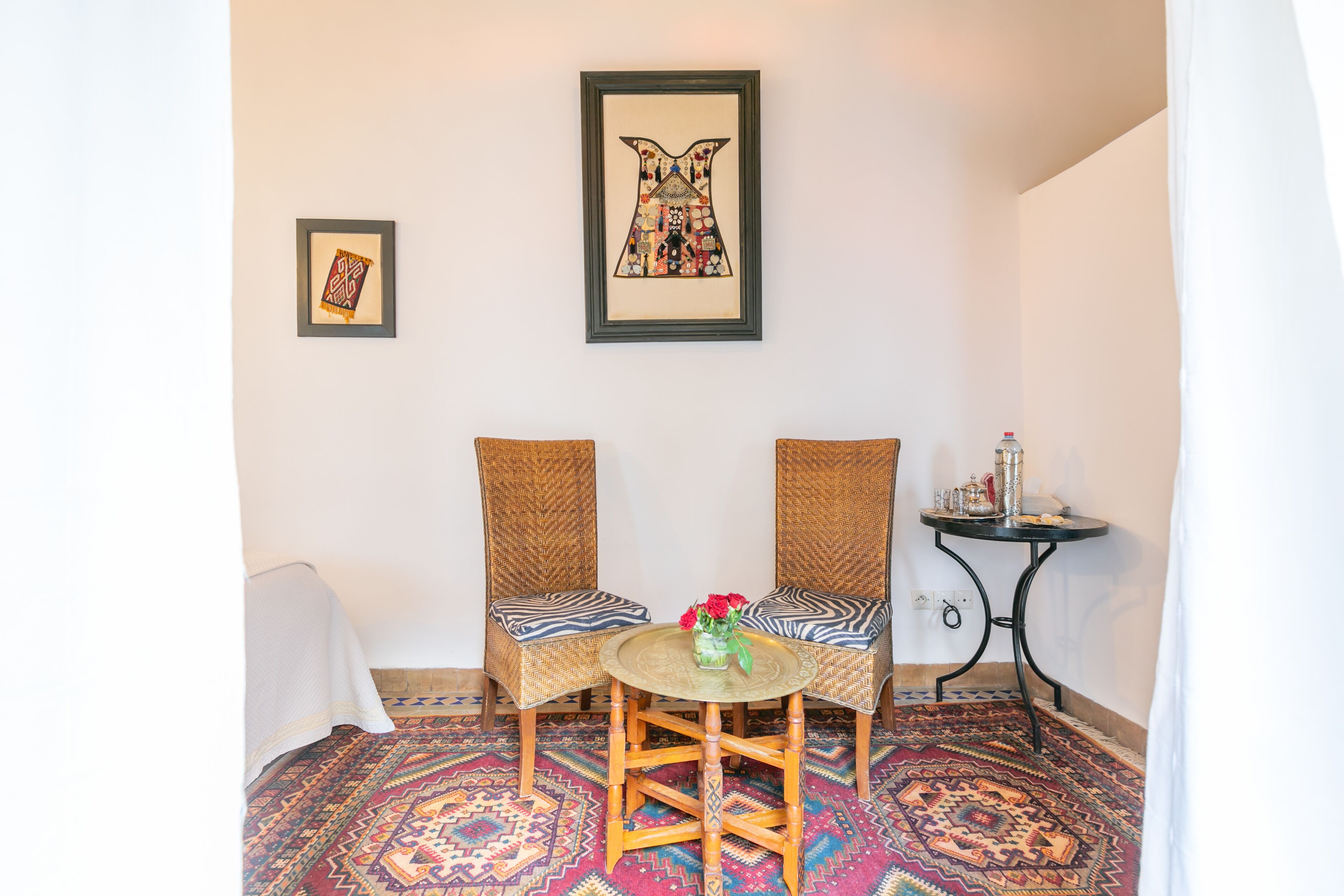 Una habitación con dos sillones de mimbre, una mesita redonda con un florero y un cuadro en la pared.