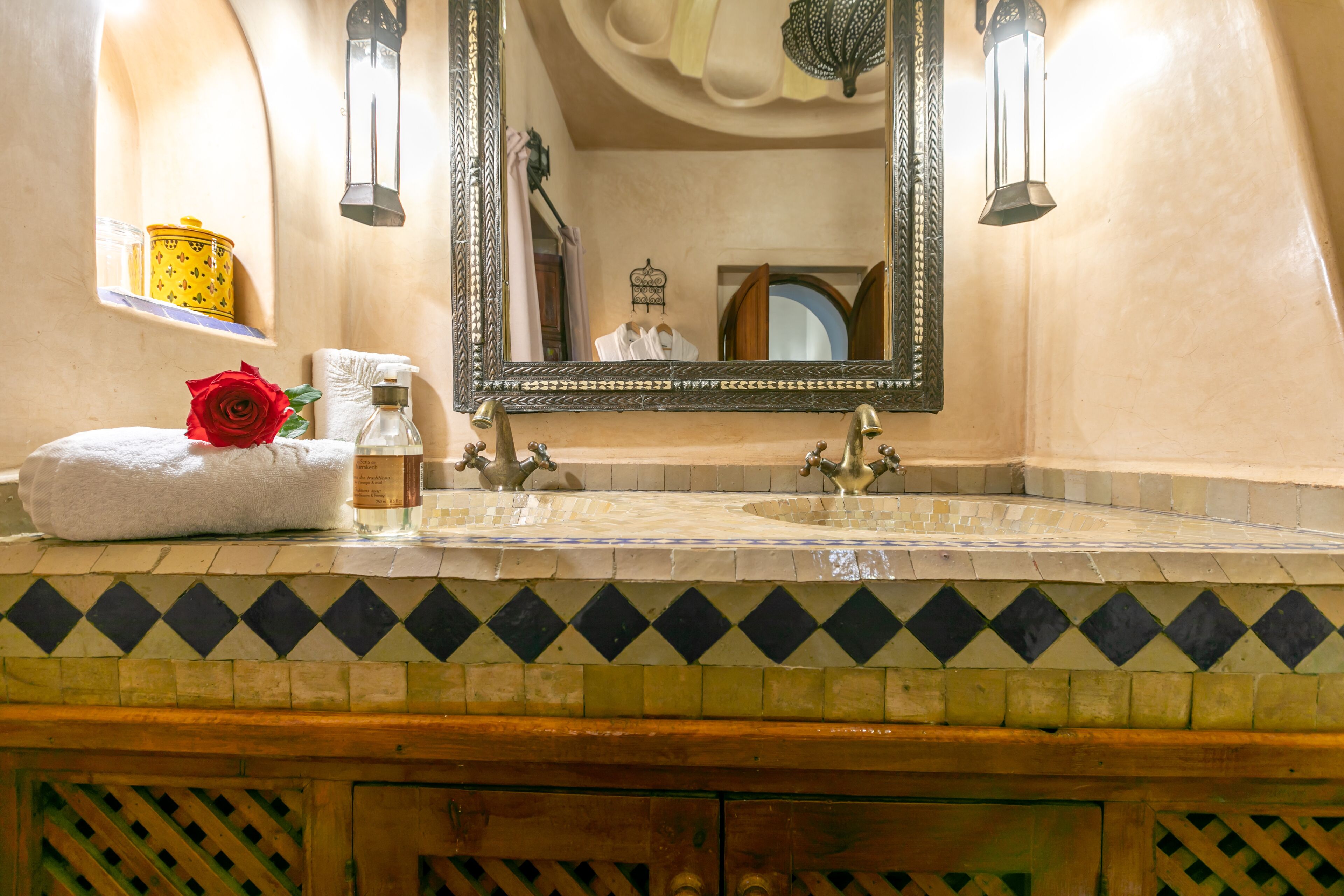Une salle de bain avec un grand miroir, deux appliques murales, un lavabo et un revêtement mural décoratif en carreaux.