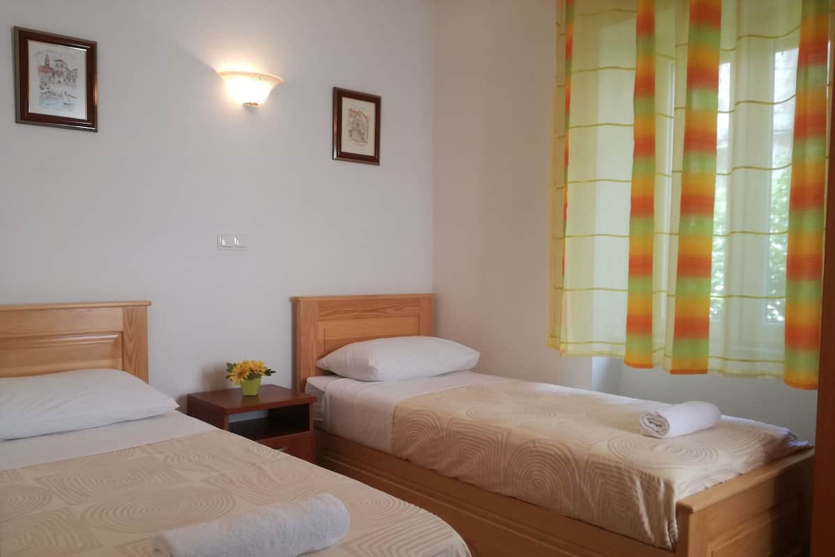 Une chambre d’hôtel avec deux lits, une table de chevet ornée d’un vase de fleurs et une fenêtre avec des rideaux colorés.