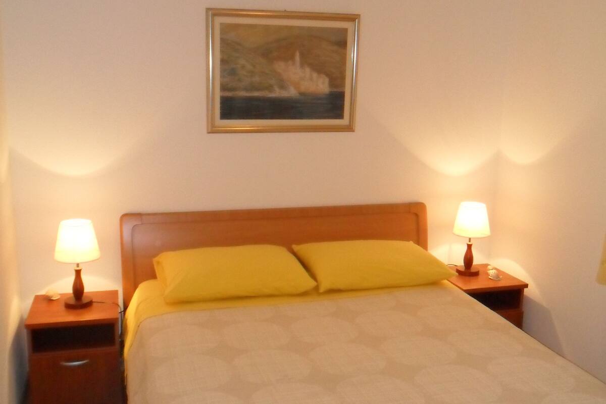 Un lit bien fait, avec une tête de lit, deux tables de chevet avec des lampes et un tableau encadré au mur.