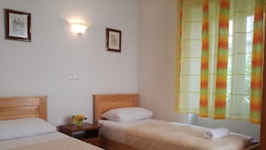 A hotel room with two beds, a nightstand with a vase of flowers, and a window with colorful curtains. - Guesthouse Ruzica (Trogir)