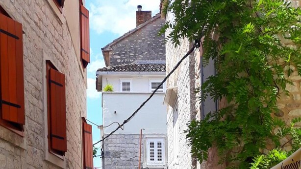 A narrow cobblestone street with stone buildings, a sign for 'Villa Ruzica' indicating rooms, and a café with outdoor seating. - Guesthouse Ruzica (Trogir)