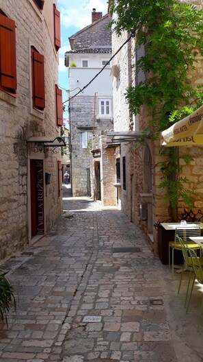 A narrow cobblestone street with stone buildings, a sign for 'Villa Ruzica' indicating rooms, and a café with outdoor seating. - Guesthouse Ruzica (Trogir)