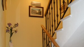 A staircase with a wooden handrail and black balusters, leading to a landing with a framed picture and a vase with flowers. - Guesthouse Ruzica (Trogir)