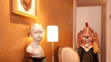 Una habitación con una mesa de madera, un busto, un maniquí vestido con traje histórico y una obra de arte enmarcada en la pared.