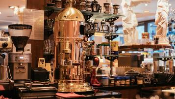 Una cafetería con una gran máquina de café espresso, estantes llenos de granos de café y una estatua de una figura vestida.