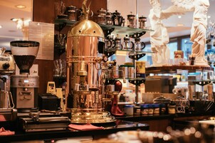 Una cafetería con una gran máquina de café espresso, estantes llenos de granos de café y una estatua de una figura vestida.